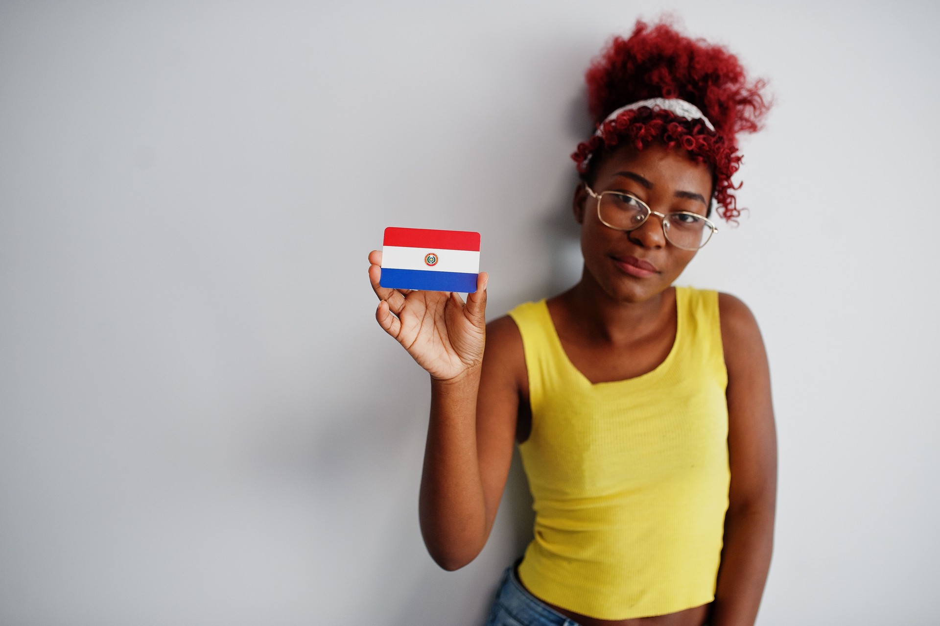African american woman with afro hair, wear yellow singlet and eyeglasses, hold Paraguay flag isolated on white background.